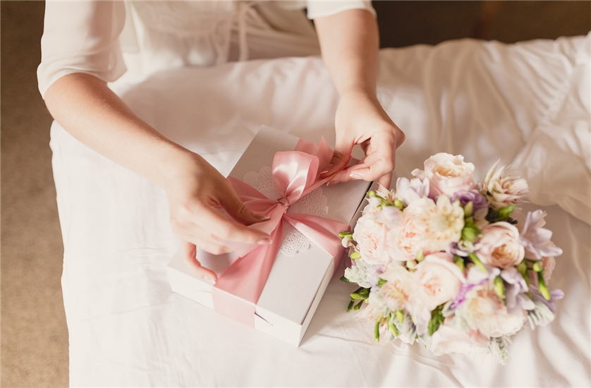 A woman ties a pink ribbon around a wedding gift. 